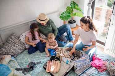 Blick von oben auf eine Familie mit zwei kleinen Töchtern, die auf dem heimischen Bett für den Urlaub packen. - HPIF07708