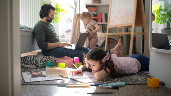 Beschäftigter Vater arbeitet mit kleinen Töchtern im Schlafzimmer, Home-Office-Konzept. - HPIF07709