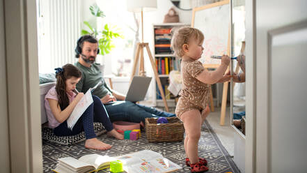 Beschäftigter Vater arbeitet mit kleinen Töchtern im Schlafzimmer, Home-Office-Konzept. - HPIF07710