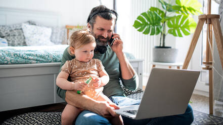 Beschäftigter Vater arbeitet mit kleinem Kleinkind Tochter im Schlafzimmer, Home-Office-Konzept. - HPIF07711