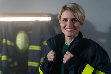 A mid adult female firefighter looking at camera indoors in fire station at night. - HPIF07730