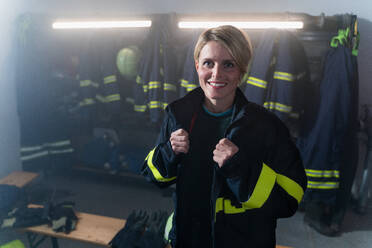 A mid adult female firefighter looking at camera indoors in fire station at night. - HPIF07731