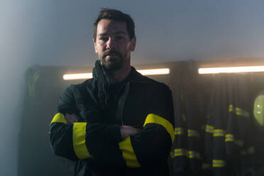 A mature firefighter in fire station at night, looking at camera. - HPIF07733