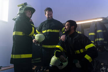 Happy firefighters men and woman talking after an action indoors in fire station - HPIF07737