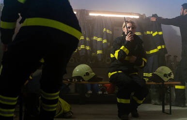 Busy firefighters men and woman getting ready for an action indoors in fire station - HPIF07738