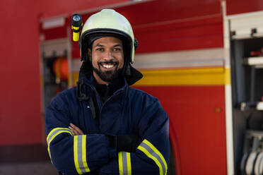 A happy young African-american firefighter man with fire truck in background. - HPIF07742