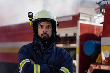 A serious young African-american firefighter man with fire truck and smoke in background. - HPIF07743