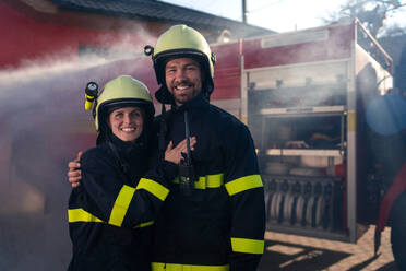 Happy firefighters man and woman after action looking at a camera with fire truck in background - HPIF07747