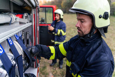 Feuerwehrmänner, die eine Sauerstoffmaske aus dem Feuerwehrauto nehmen, draußen in der Natur. - HPIF07756