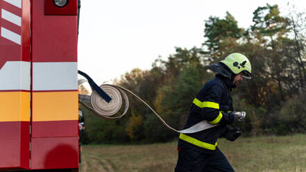 A firefighter at action taking hose from fire truck outdoors in nature. - HPIF07757