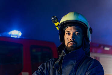 A portrait of dirty firefighter man on duty with fire truck in background at night, smiling. - HPIF07765