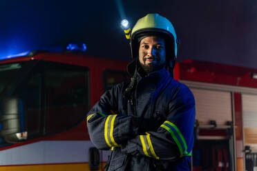 A portrait of dirty firefighter man on duty with fire truck in background at night, smiling. - HPIF07766
