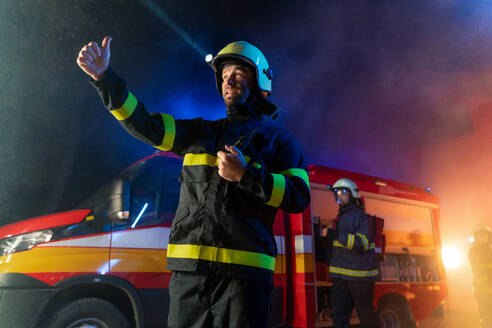 Eine niedrige Winkel Ansicht von m Feuerwehrmann im Gespräch mit Walkie Talkie mit Feuer LKW im Hintergrund in der Nacht. - HPIF07774