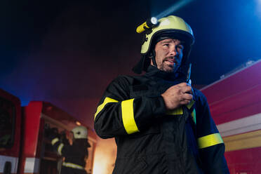 Eine niedrige Winkel Ansicht von m Feuerwehrmann im Gespräch mit Walkie Talkie mit Feuer LKW im Hintergrund in der Nacht. - HPIF07779