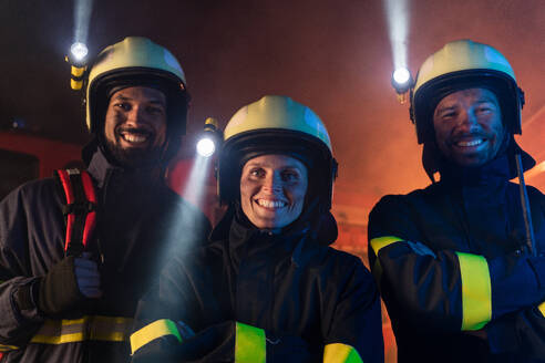 Firefighters men and woman looking at camera with a fire truck in background at night. - HPIF07790