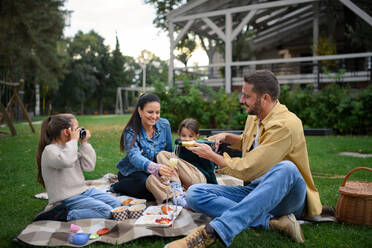 Eine glückliche junge Familie sitzt auf einer Decke und macht ein Picknick zum Mitnehmen im Freien in einem Restaurant. - HPIF07795