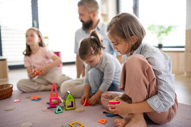 A father with three daughters indoors at home, playing on floor. - HPIF07797