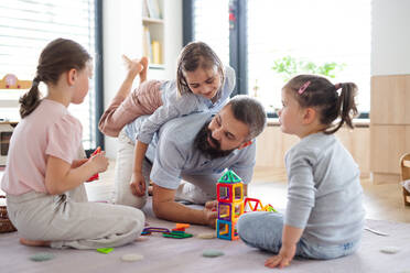 A father with three daughters indoors at home, playing on floor. - HPIF07800