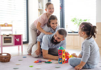 A father with three daughters indoors at home, playing on floor. - HPIF07801