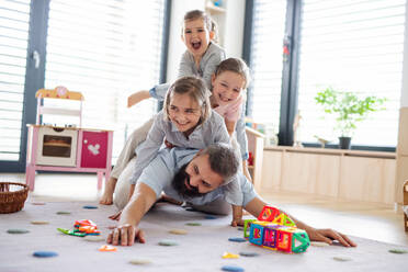 A father with three daughters indoors at home, playing on floor. - HPIF07802