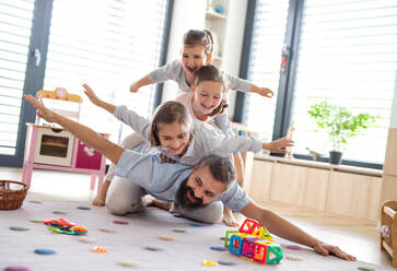 A father with three daughters indoors at home, playing on floor. - HPIF07803