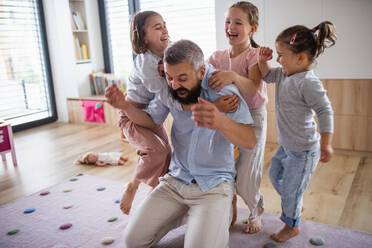 A father with three daughters indoors at home, playing on floor. - HPIF07805