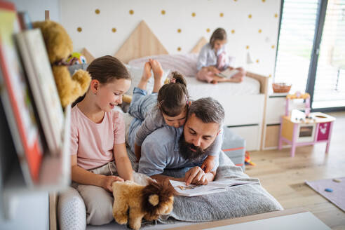 Ein Vater mit drei Töchtern sitzt zu Hause und liest ein Buch. - HPIF07808