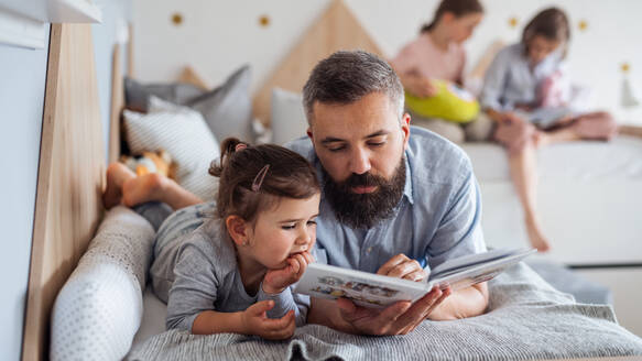 Ein Vater mit drei Töchtern sitzt zu Hause und liest ein Buch. - HPIF07809