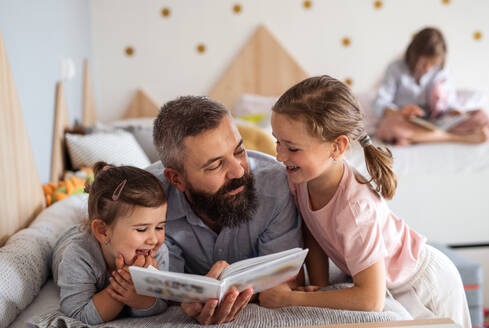 Ein Vater mit drei Töchtern sitzt zu Hause und liest ein Buch. - HPIF07810
