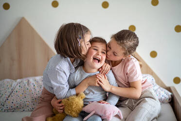 A portrait of three girls sisters indoors at home, kissing. - HPIF07814