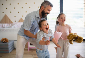 A father with three daughters indoors at home, having fun playing. - HPIF07819