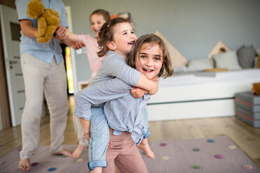 An unrecognizable father with three daughters indoors at home, playing and having fun. - HPIF07824