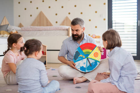 A father with three daughters indoors at home, playing on floor. - HPIF07830
