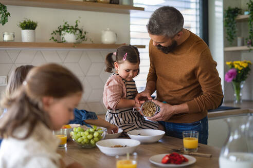 Ein Vater mit drei Töchtern zu Hause, der in der Küche frühstückt. - HPIF07834