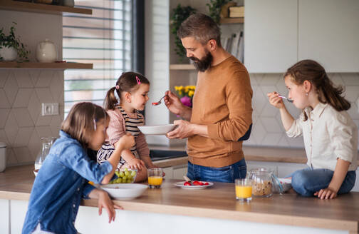 Ein Vater mit drei Töchtern zu Hause, der in der Küche frühstückt. - HPIF07835