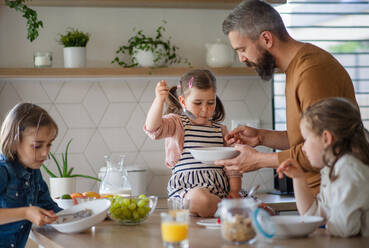 Ein Vater mit drei Töchtern zu Hause, der in der Küche frühstückt. - HPIF07836