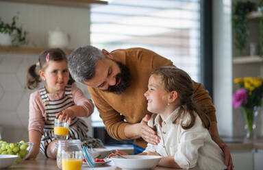 Ein Vater mit drei Töchtern zu Hause, der in der Küche frühstückt. - HPIF07837