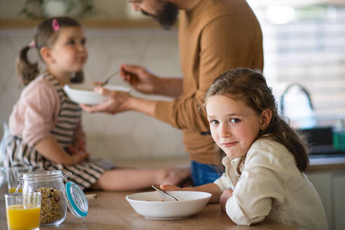 A father with daughters indoors at home, eating breakfast in kitchen. - HPIF07838