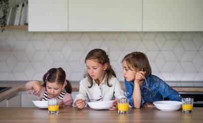 A portrait of three girls sisters indoors at home, eating breakfast. - HPIF07839