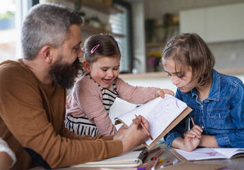 A father with daughters indoors at home, drawing pictures. - HPIF07843