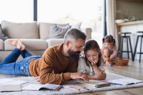 Mature father with daughters indoors at home, drawing pictures on floor. - HPIF07844