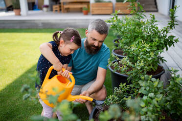 A father and small daughter with watering can outdoors in tha backyard, looking at camera. - HPIF07846