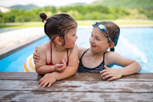 Porträt von zwei kleinen Mädchen Schwestern im Freien im Hinterhof, im Schwimmbad sprechen. - HPIF07848