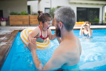 Vater mit glücklichen Töchtern draußen im Garten, die im Swimmingpool spielen. - HPIF07849