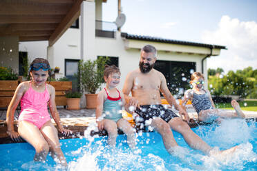 Ein Vater mit drei Töchtern im Garten, am Swimmingpool sitzend. - HPIF07851