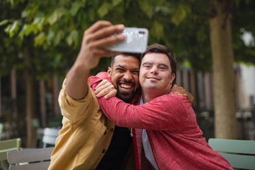 Ein junger Mann mit Down-Syndrom und sein Mentor genießen ein Selfie in einem Straßencafé - HPIF07861