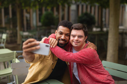 Ein junger Mann mit Down-Syndrom und sein Mentor machen ein Selfie, während sie in einem Café sitzen - HPIF07862