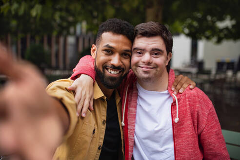 Ein junger Mann mit Down-Syndrom und sein Mentor machen ein Selfie und lächeln für die Kamera in der freien Natur - HPIF07864