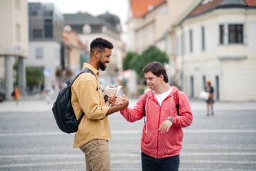 Ein junger Mann mit Down-Syndrom und sein betreuender Freund treffen sich draußen in der Stadt und grüßen sich - HPIF07877