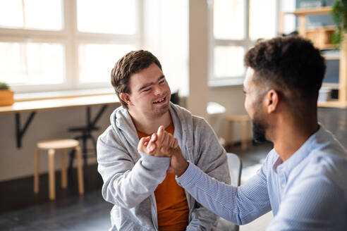 A young happy man with Down syndrome with his mentoring friend celebrating success indoors at school. - HPIF07896